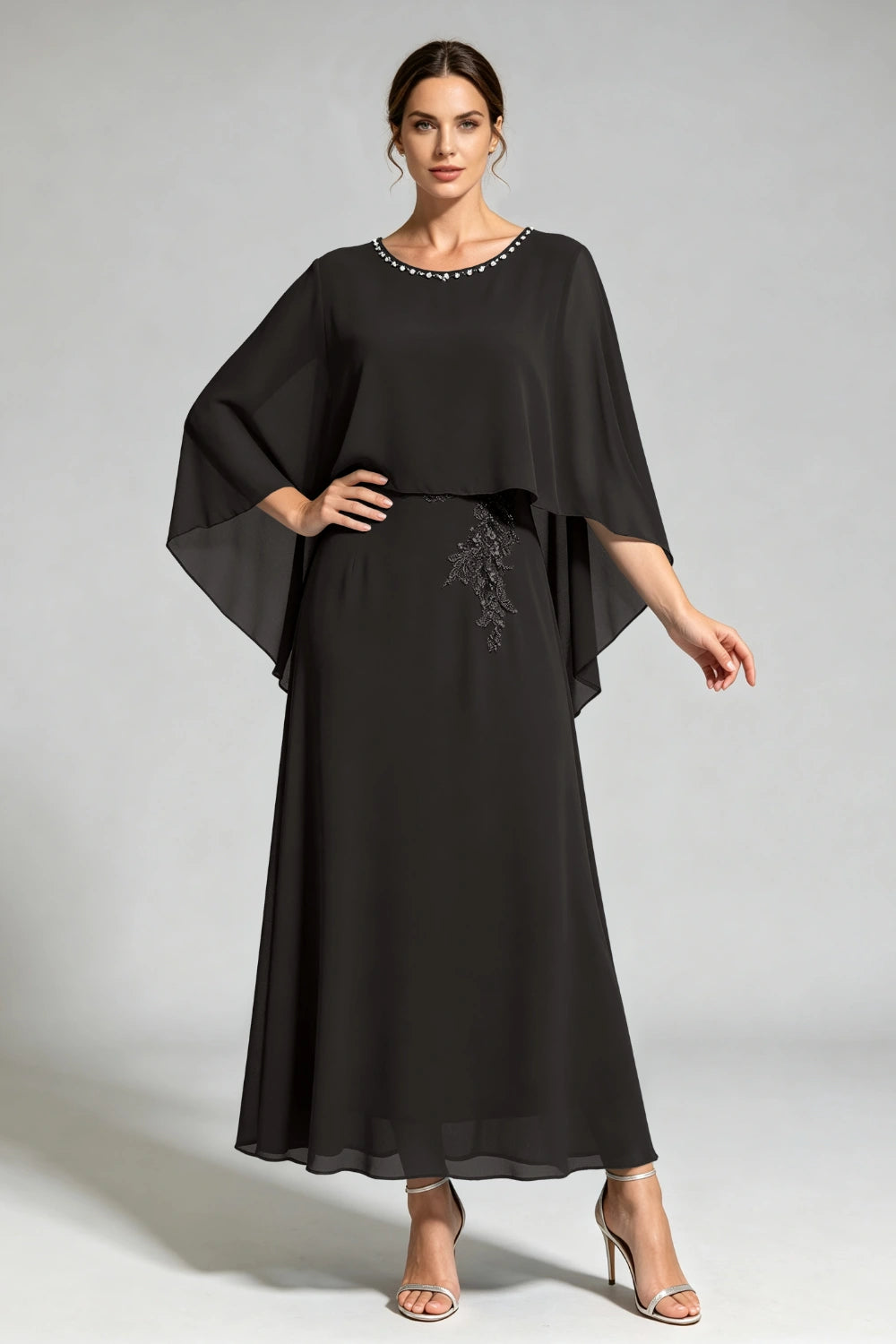 Front view of the black cape dress with a beaded round neckline and tonal floral applique.