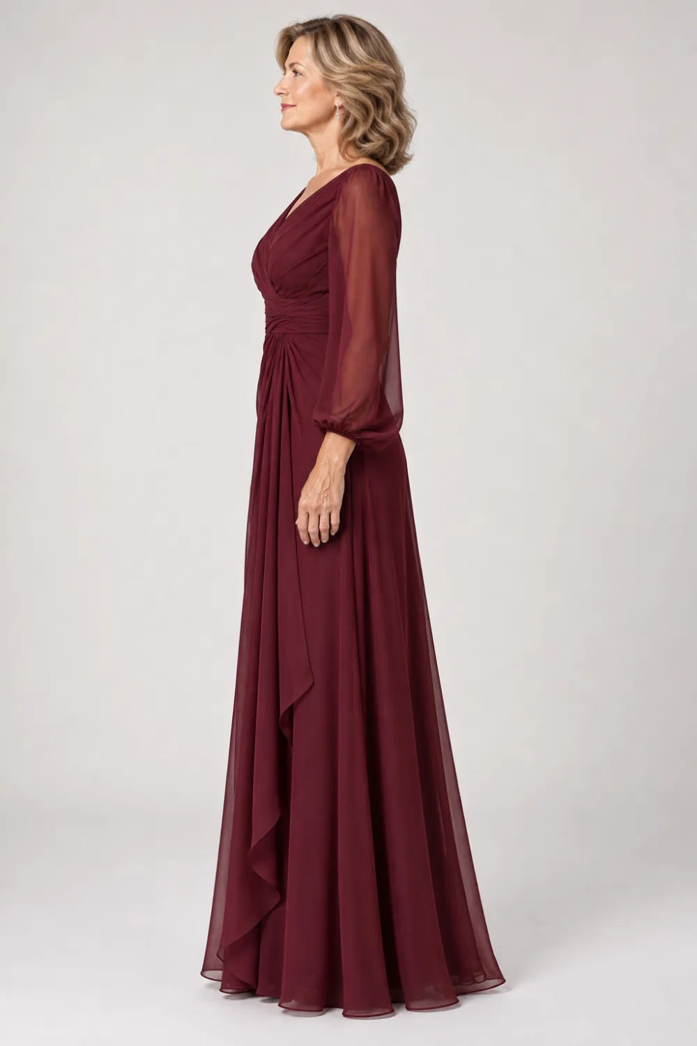 Burgundy dress with crossover bodice, gathered waist and cascading side panel, side view.