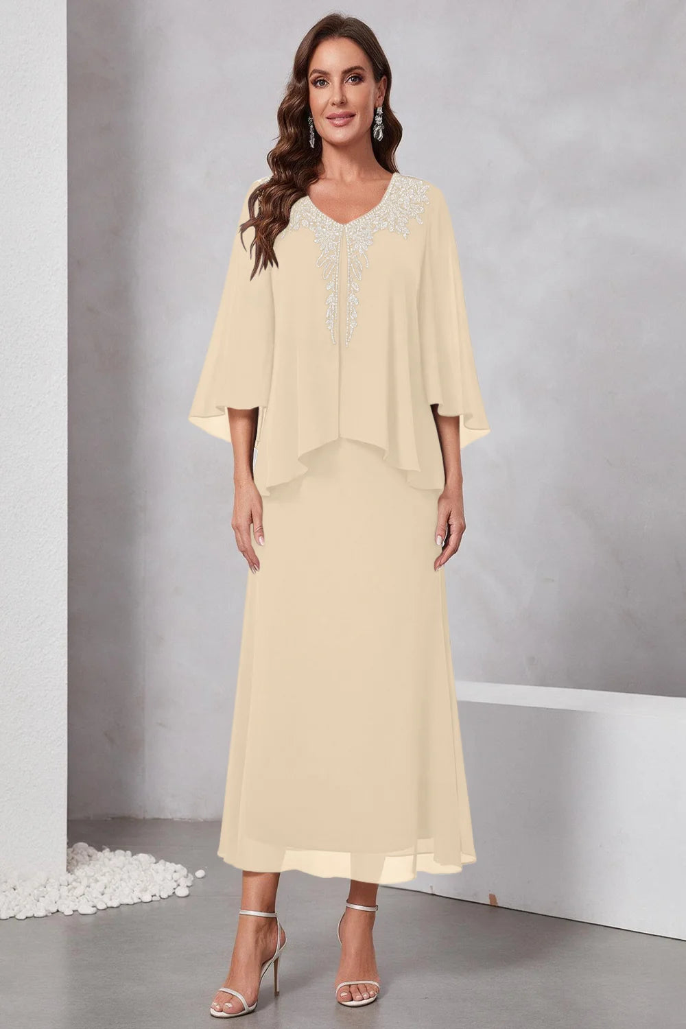 Front view of a champagne dress with a decorated neckline and short upper overlay.