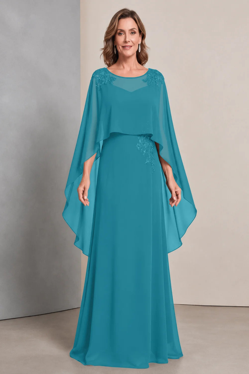 Front view of a teal dress with a sheer neckline and long cape sides.