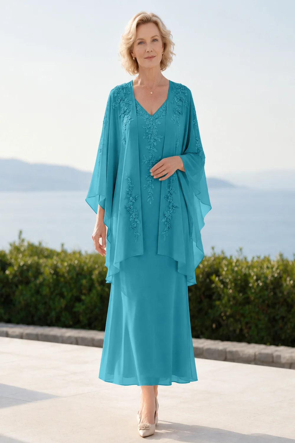Front view of a teal dress with a decorated neckline and long upper overlay.