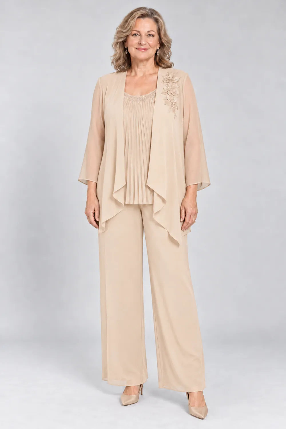 Champagne pant suit with fine pleats, decorated neckline and floral shoulder motif, front view.