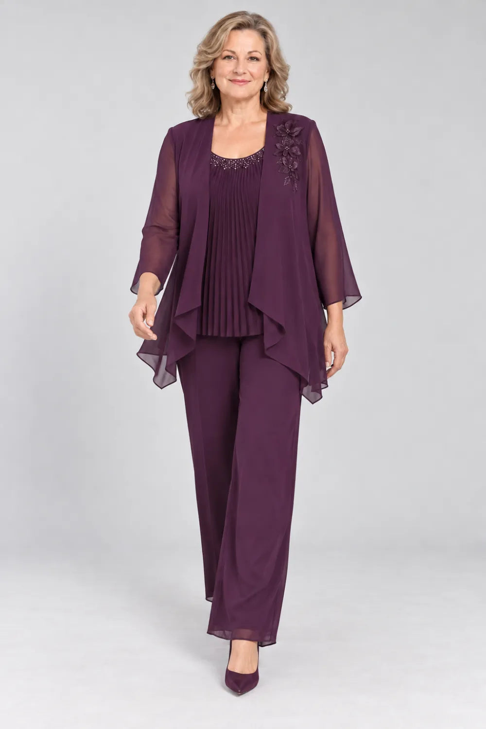 Plum pant suit with fine pleats, decorated neckline and floral shoulder motif, posed front view.