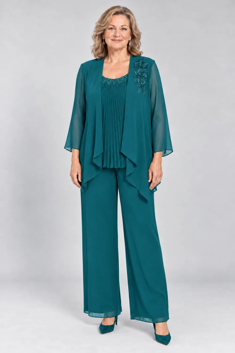 Teal pant suit with fine pleats, decorated neckline and floral shoulder motif, front view.