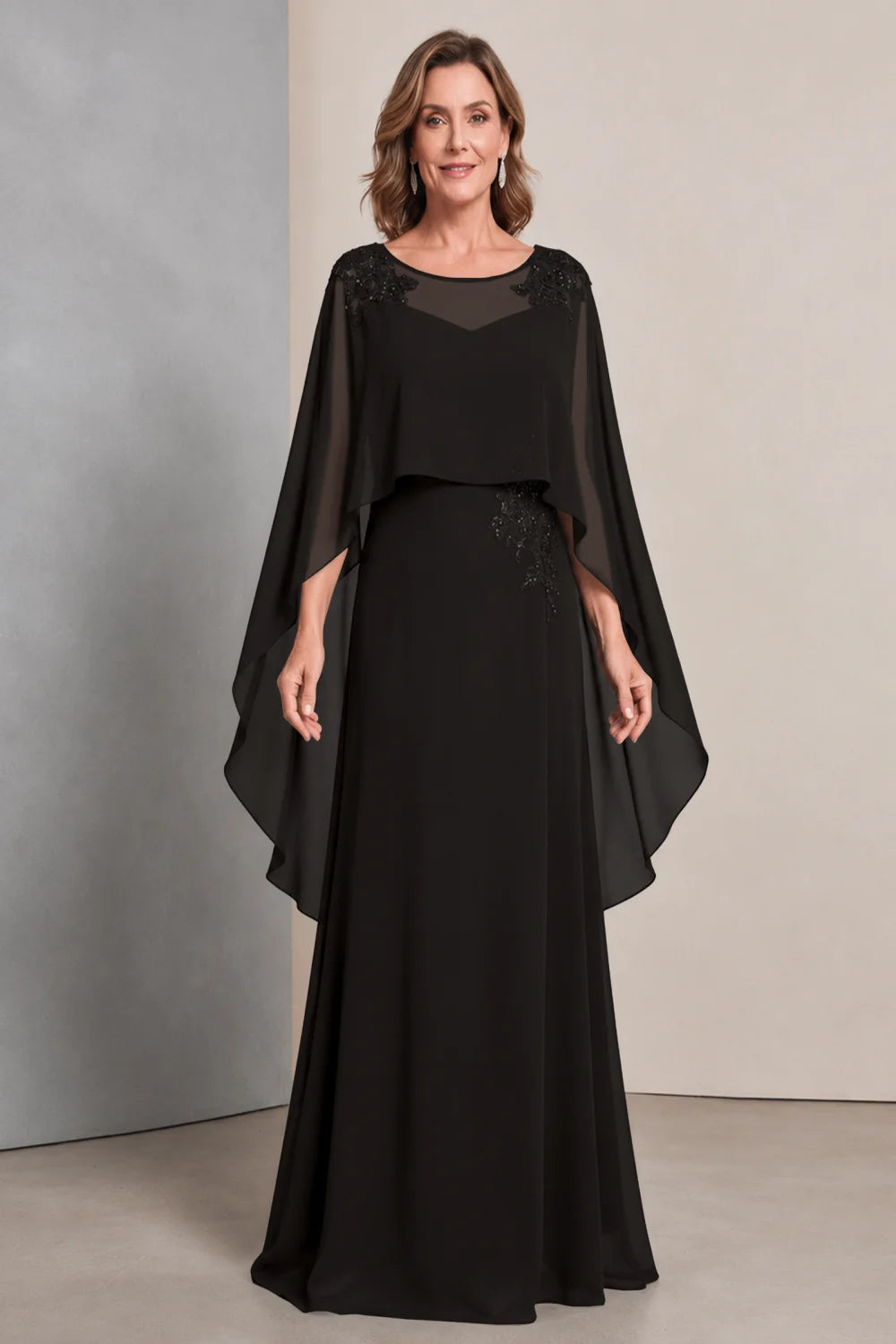 Front view of a black dress with a sheer neckline and long cape sides.