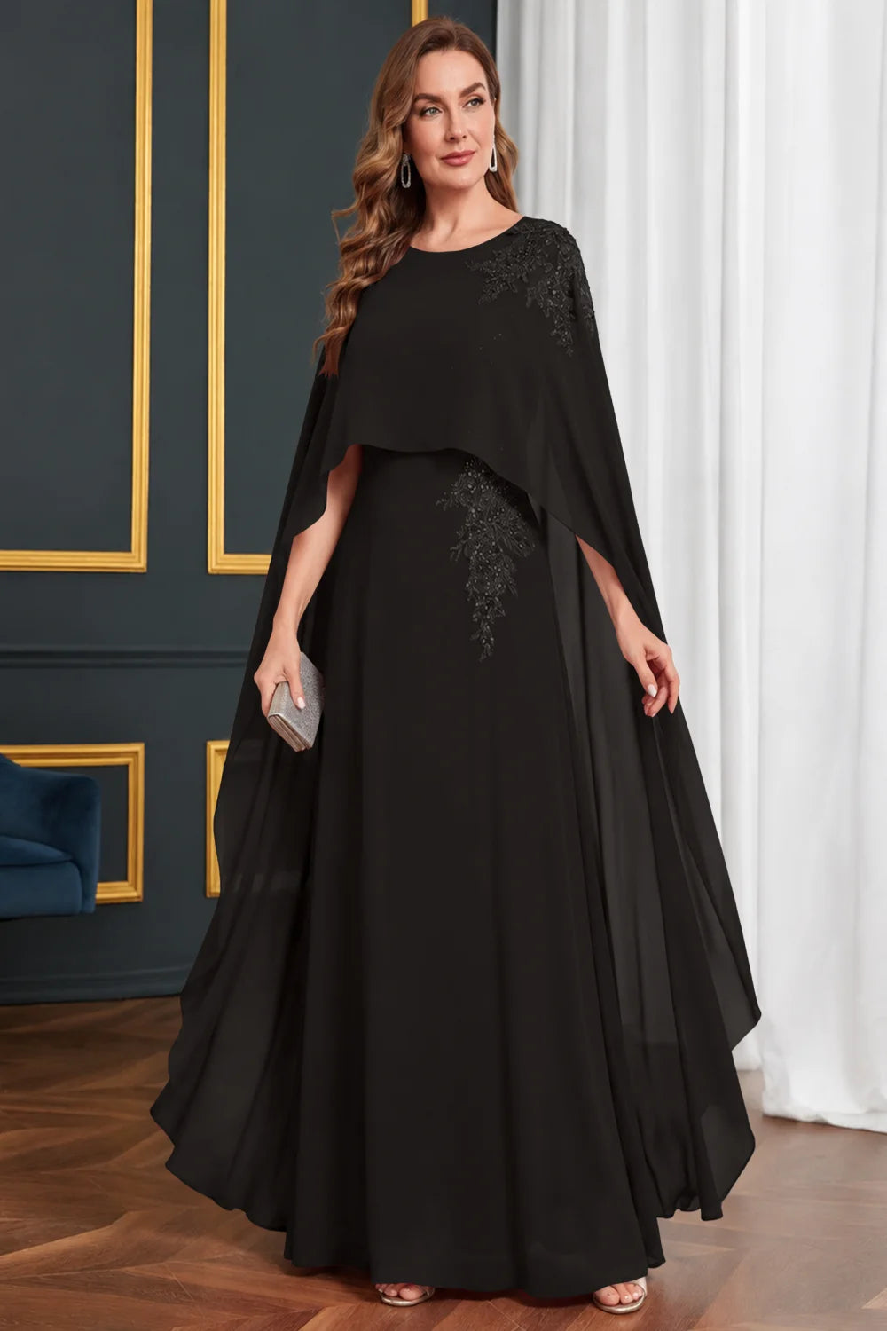 Front view of a black dress with long cape panels and shoulder decoration.