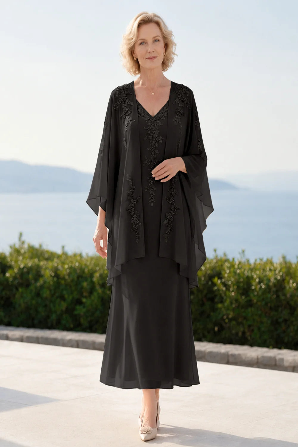 Front view of a black dress with a decorated neckline and long upper overlay.