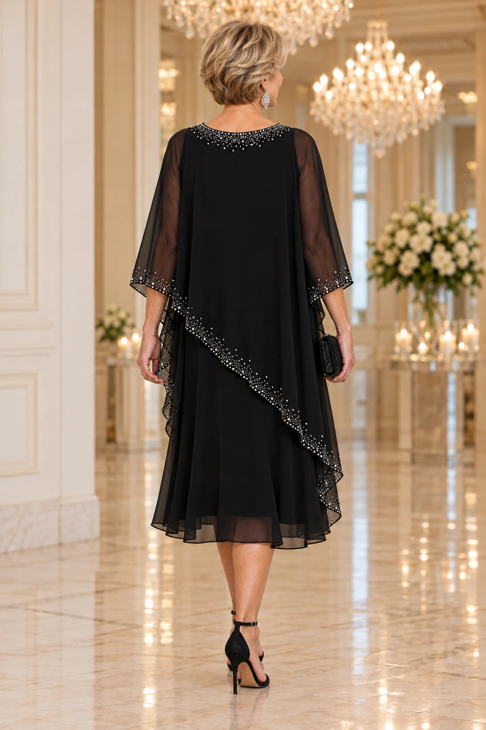 Direct back view of the black midi dress showing the decorated rear neckline and diagonal sheer cape edge.