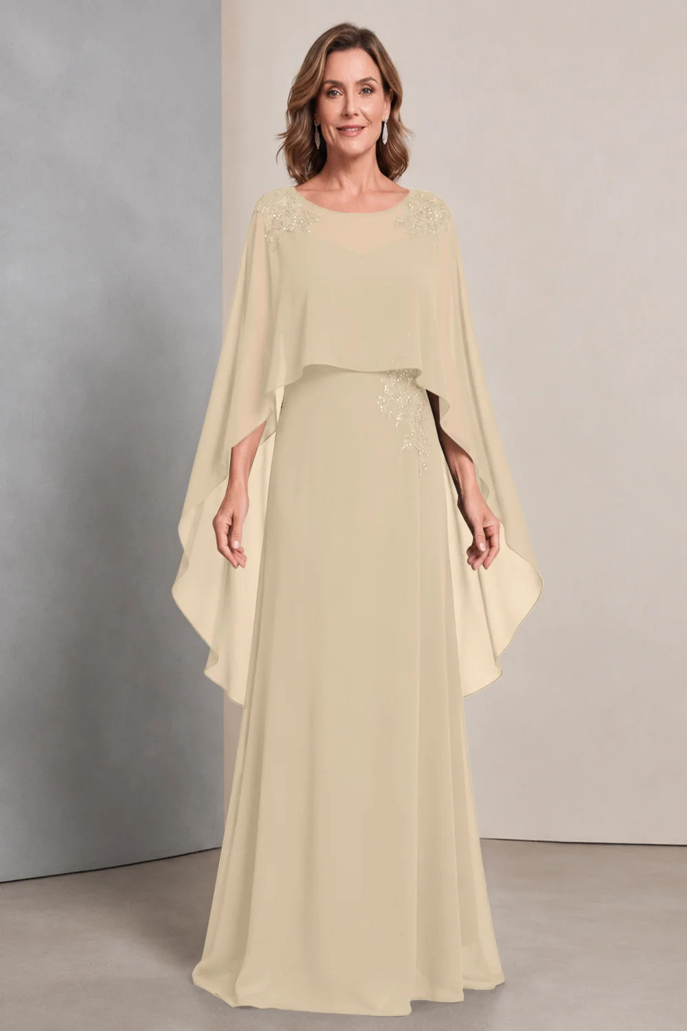 Front view of a champagne dress with a sheer neckline and long cape sides.