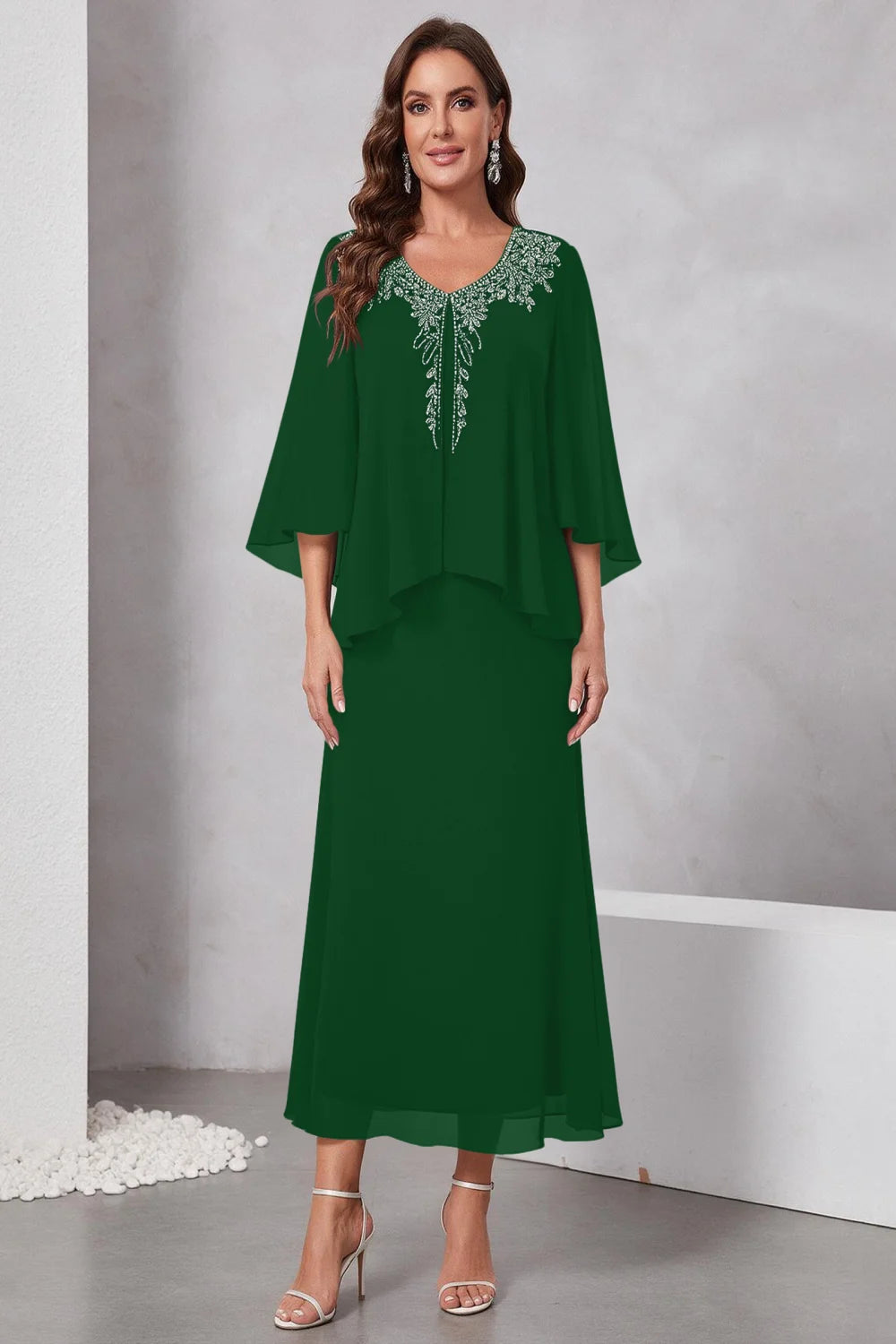 Front view of a emerald green dress with a decorated neckline and short upper overlay.
