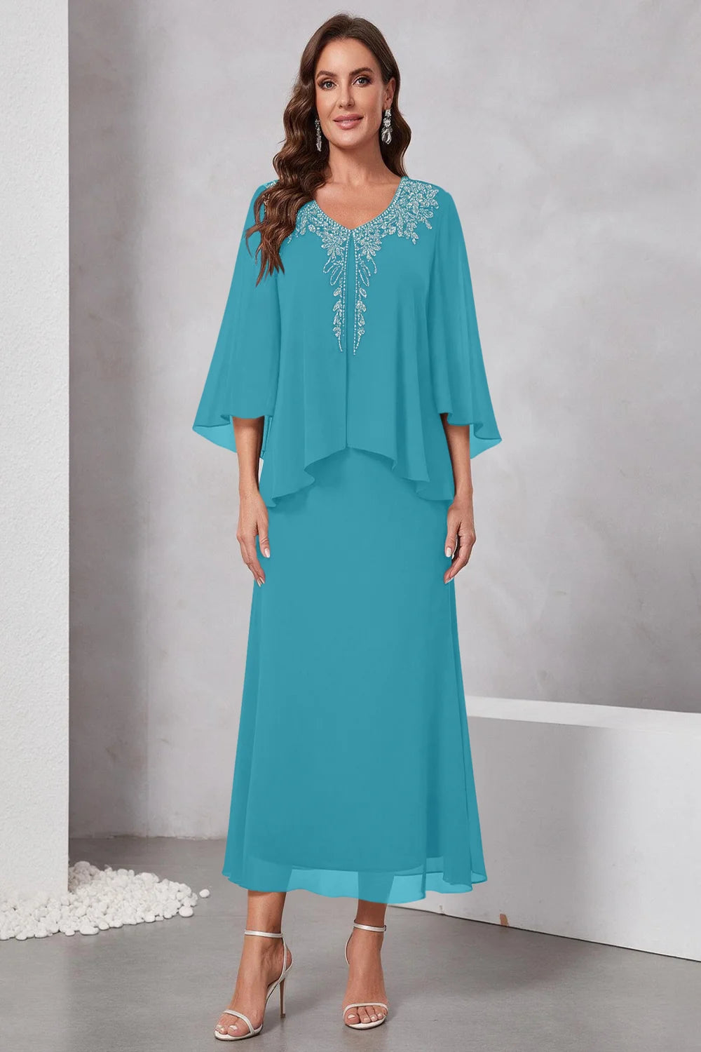 Front view of a teal dress with a decorated neckline and short upper overlay.