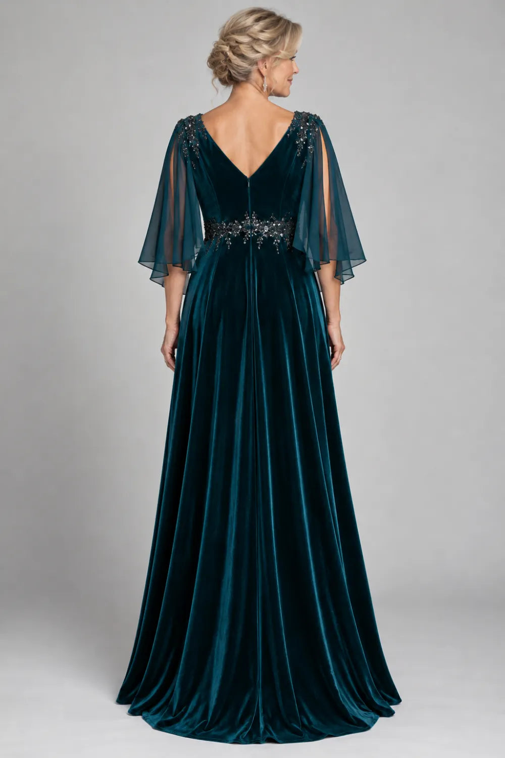 Back view of a teal floor-length gown with sheer open cape sleeves.