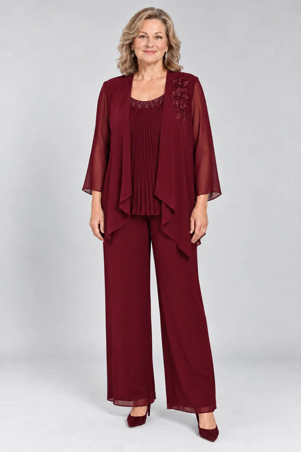 Burgundy pant suit with fine pleats, decorated neckline and floral shoulder motif, front view.