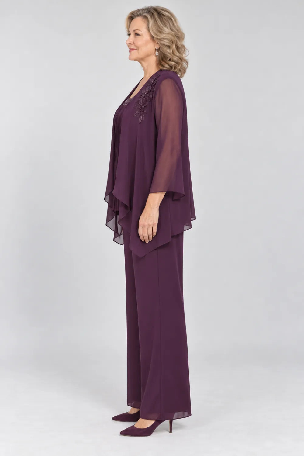Plum pant suit with fine pleats, decorated neckline and floral shoulder motif, side view.