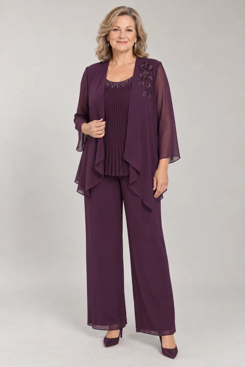 Plum pant suit with fine pleats, decorated neckline and floral shoulder motif, front view.