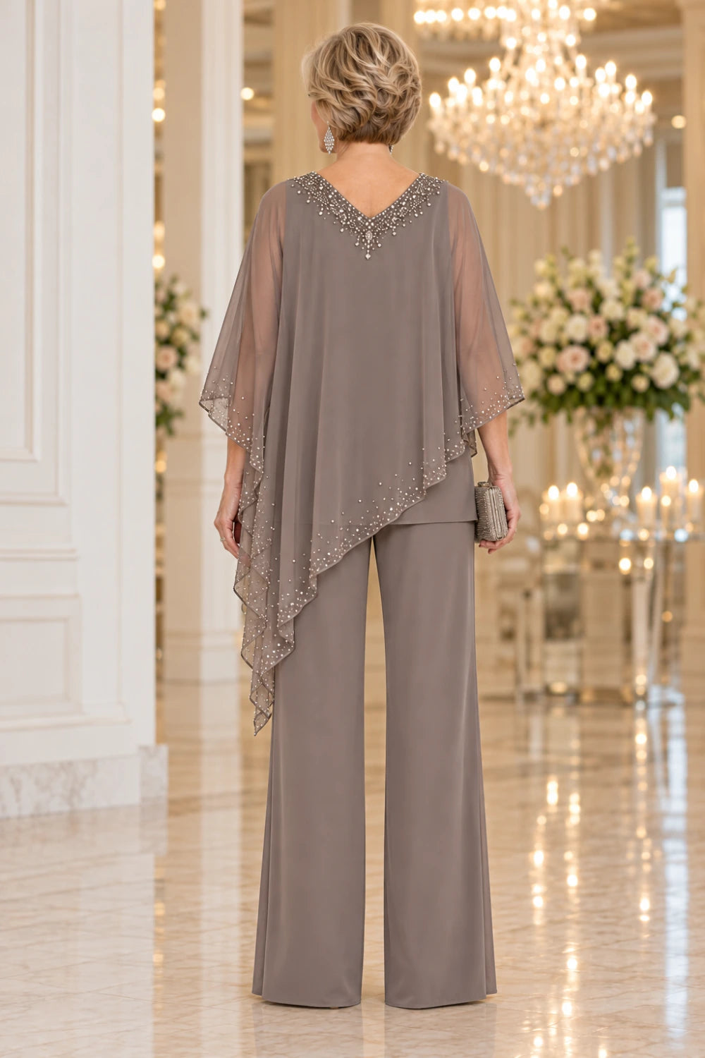 Back view of the taupe pant suit showing the decorated rear V neckline, diagonal cape edge and wide trouser legs.