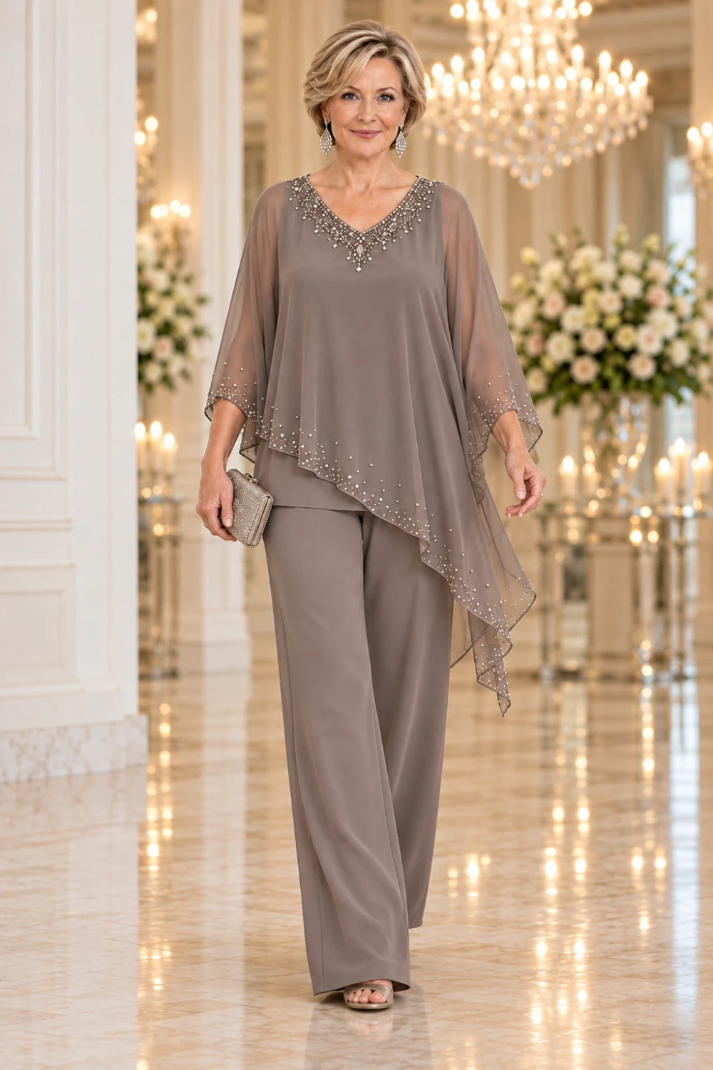 Walking front view of the taupe trouser outfit with a pointed sheer cape and wide-leg pants.